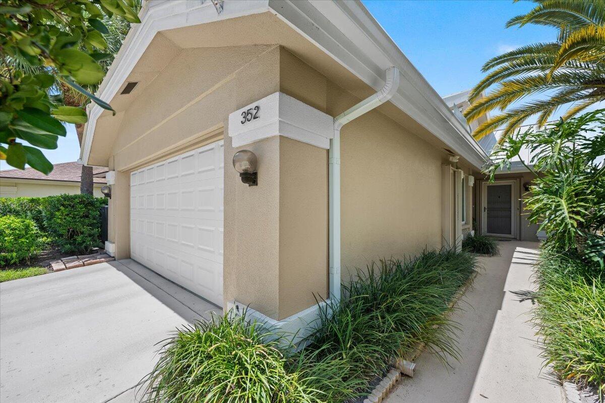 A tan house exterior features a white garage door, a walkway, and a palm tree — 352 River Edge Road, Jupiter FL 33477, JUPITER, FL