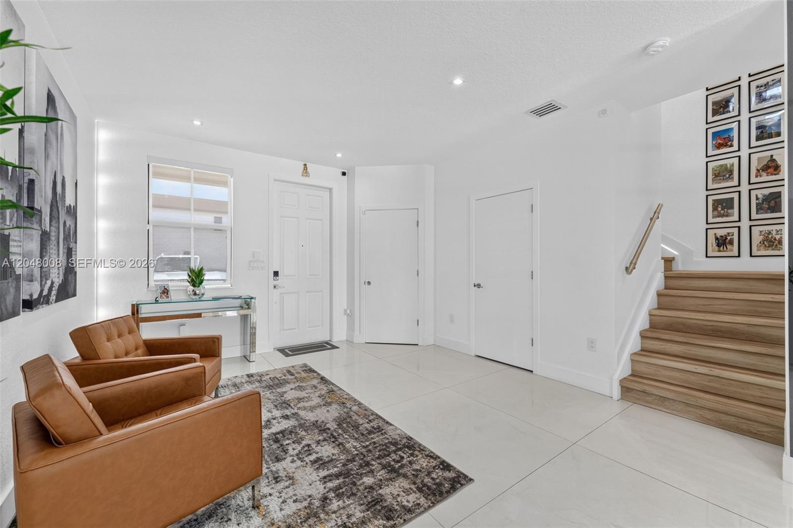 A bright entryway features white tile floors, two leather armchairs, and a wooden staircase — 11024 W 35th Ln, Hialeah FL 33018, HIALEAH, FL