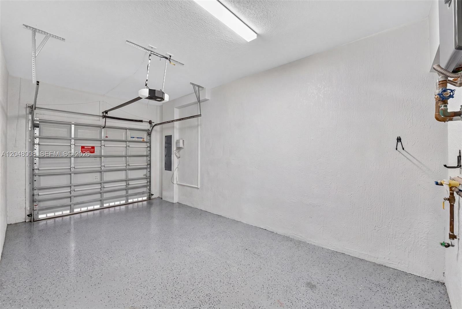A clean garage features a speckled epoxy floor, white walls, and a metal roll-up door — 11024 W 35th Ln, Hialeah FL 33018, HIALEAH, FL