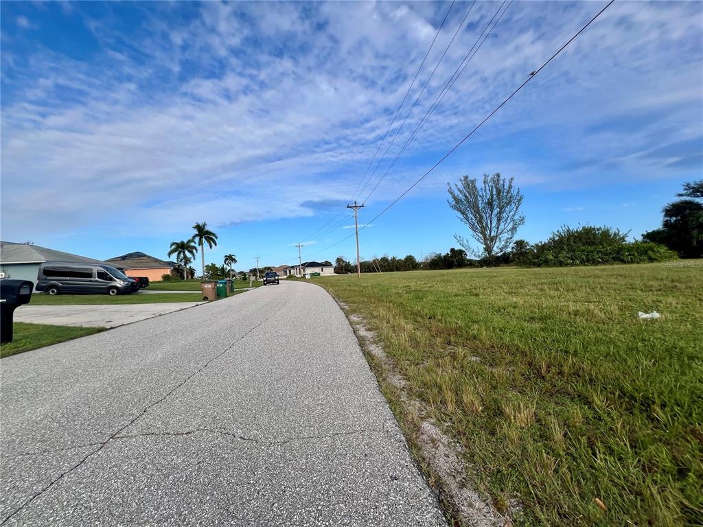 A paved road runs alongside a large, grassy vacant lot under a blue sky — 1857 NE 23RD STREET, CAPE CORAL, FL