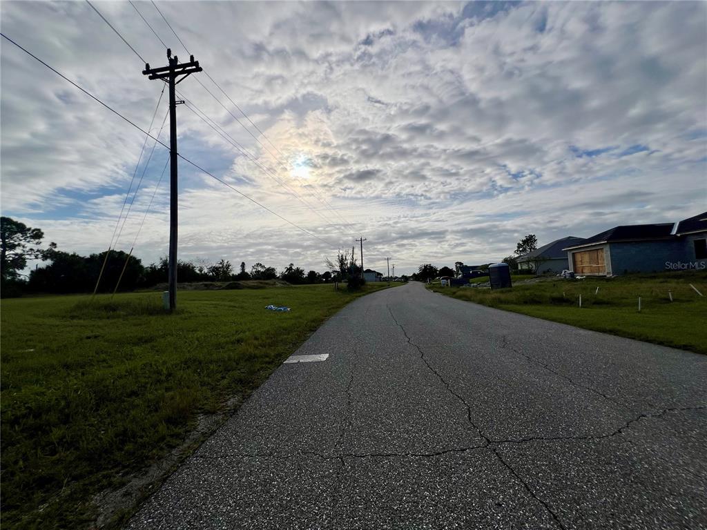 A paved road stretches through a grassy residential area with utility poles under a cloudy sky — 1857 NE 23RD STREET, CAPE CORAL, FL