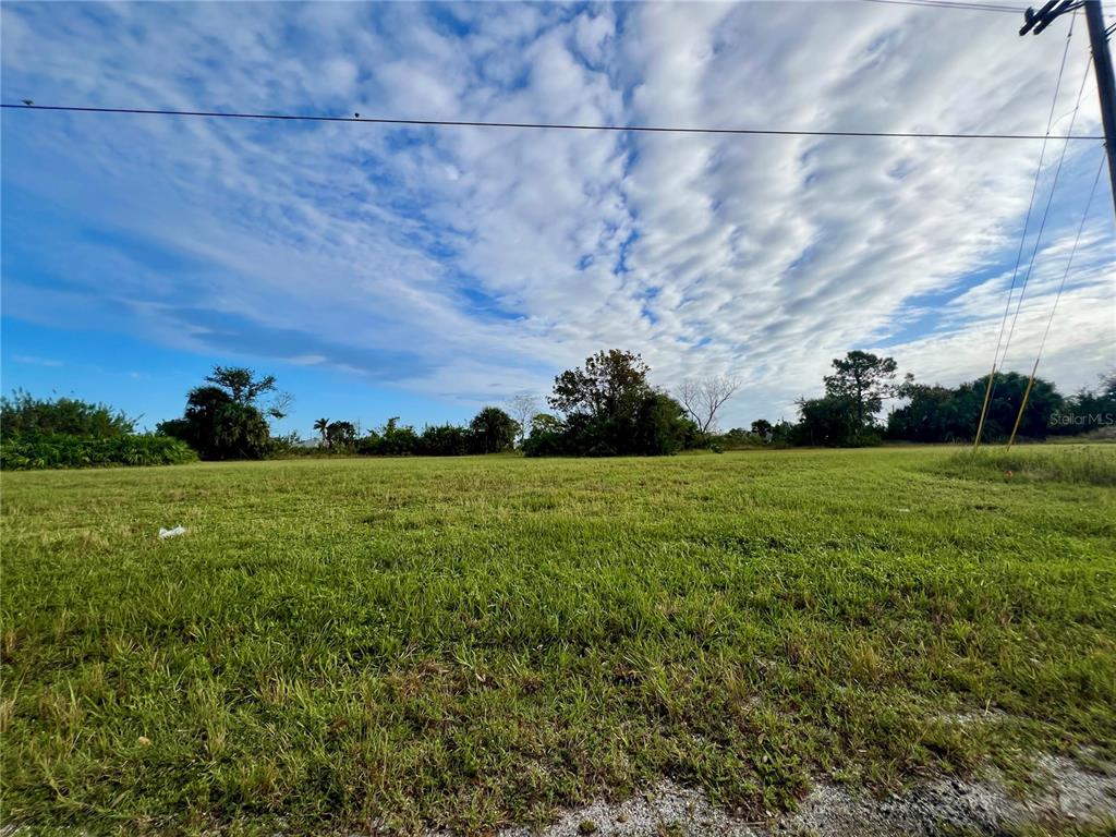 A wide, grassy vacant lot under a blue sky with scattered clouds — 1857 NE 23RD STREET, CAPE CORAL, FL
