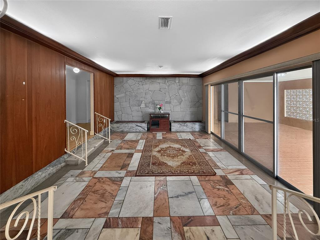 A sunken living room features marble tile flooring, wood-paneled walls, and a stone accent wall — 305 N GLEN AVENUE, TAMPA, FL