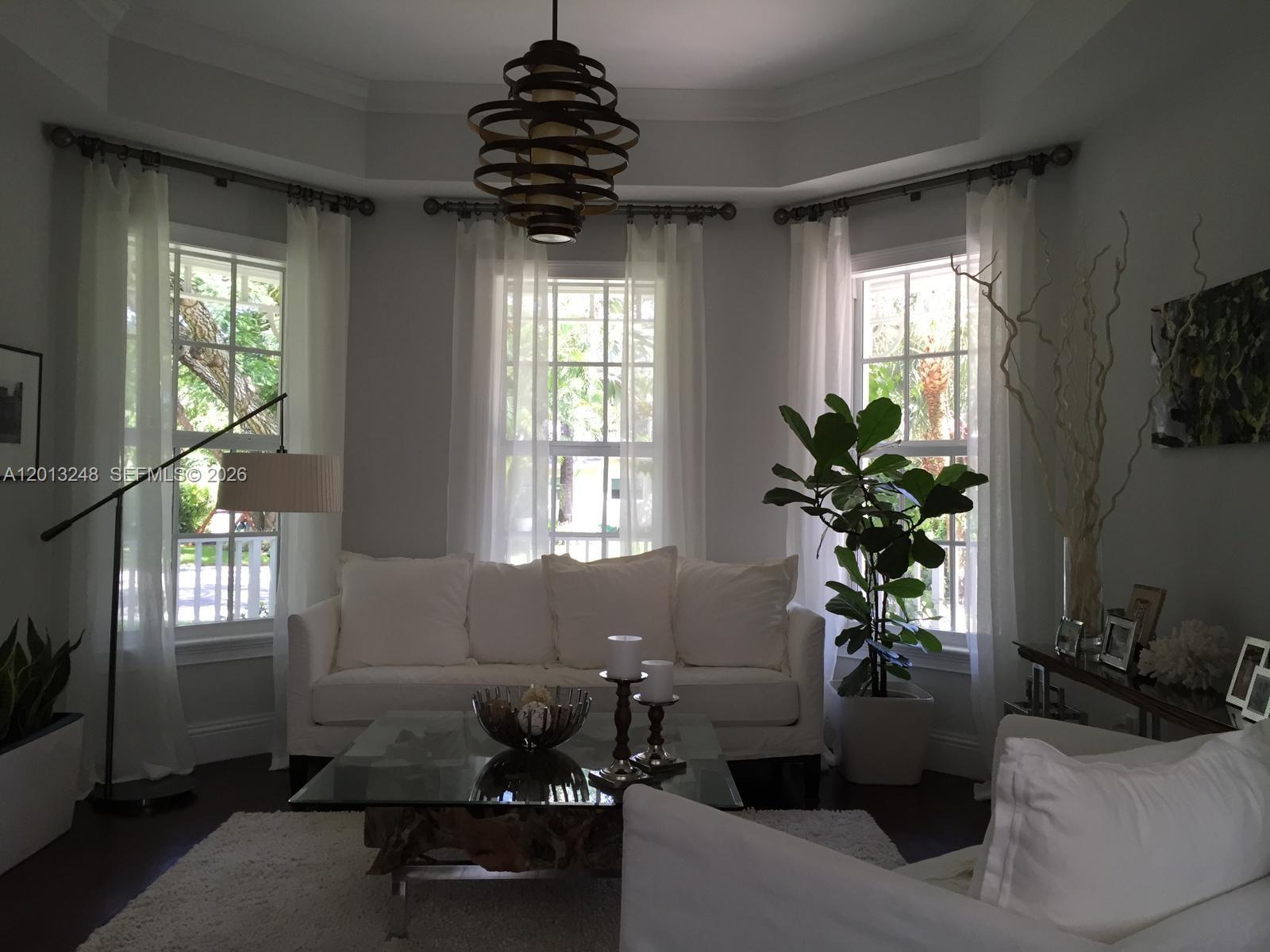A bright living room features a white sofa, glass coffee table, and large bay windows — 5000 SW 73rd Ter, Miami FL 33143, MIAMI, FL