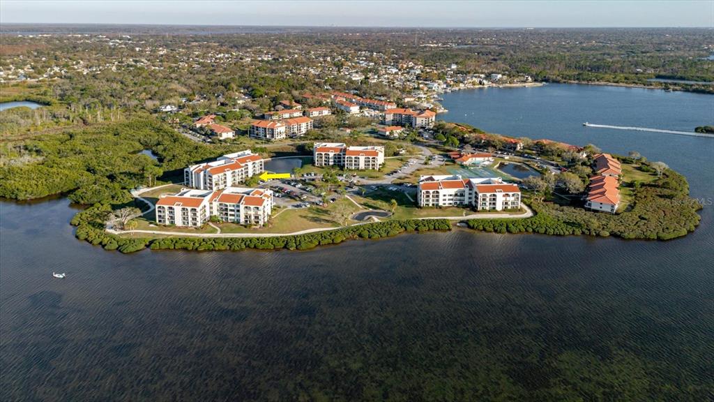 An aerial view shows a waterfront condominium complex surrounded by mangroves and a large bay — 208 MARINER DRIVE UNIT 208, TARPON SPRINGS, FL