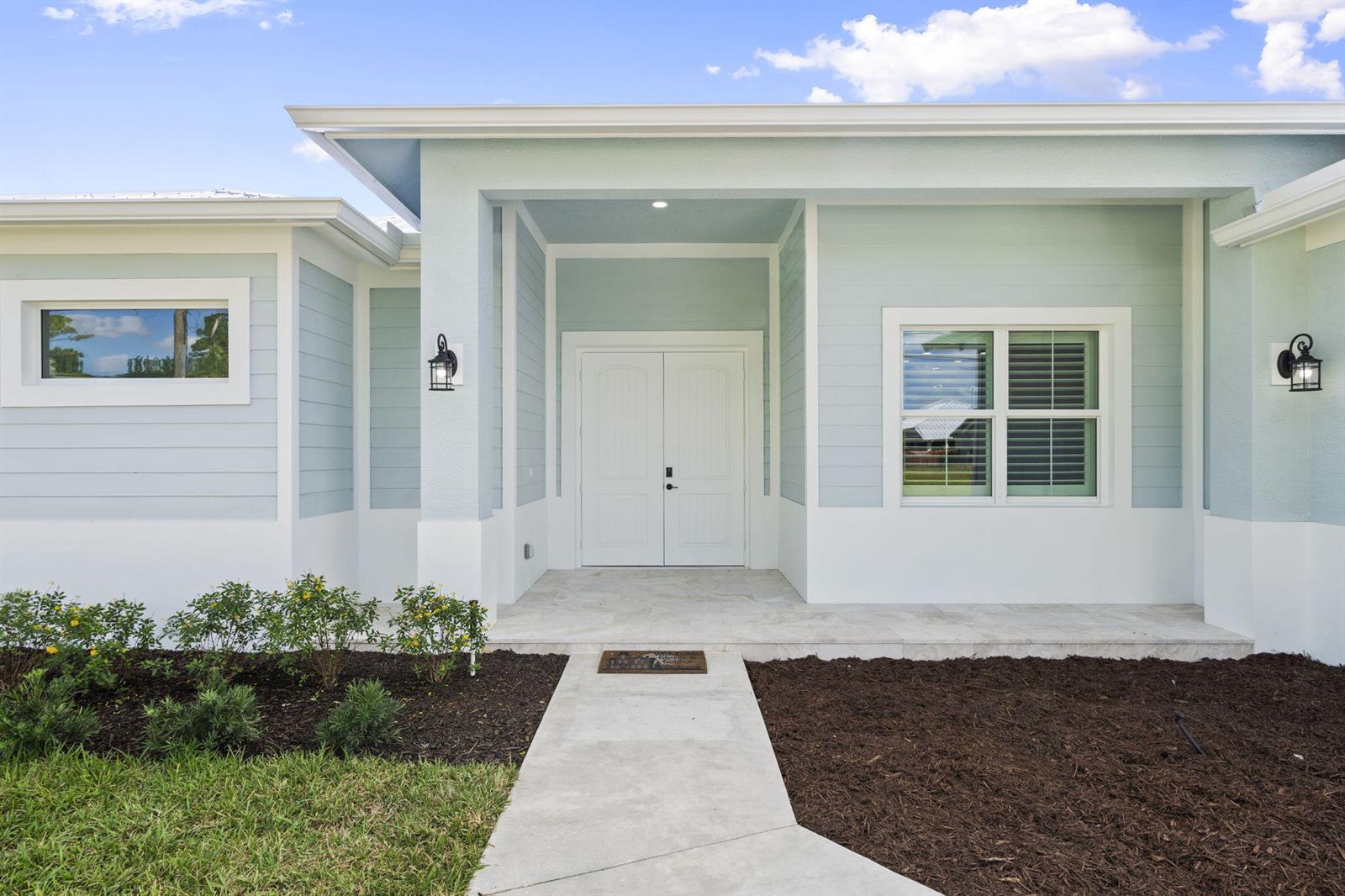 The exterior of a light blue house features a double front door and stone porch — 3834 NE Barbara Drive, Jensen Beach FL 34957, JENSEN BEACH, FL