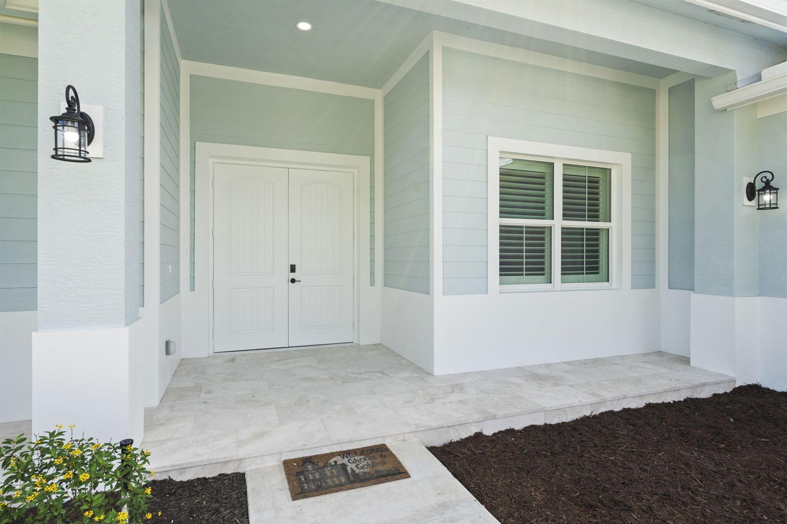 A light blue house exterior features a covered porch, double white doors, and a window — 3834 NE Barbara Drive, Jensen Beach FL 34957, JENSEN BEACH, FL