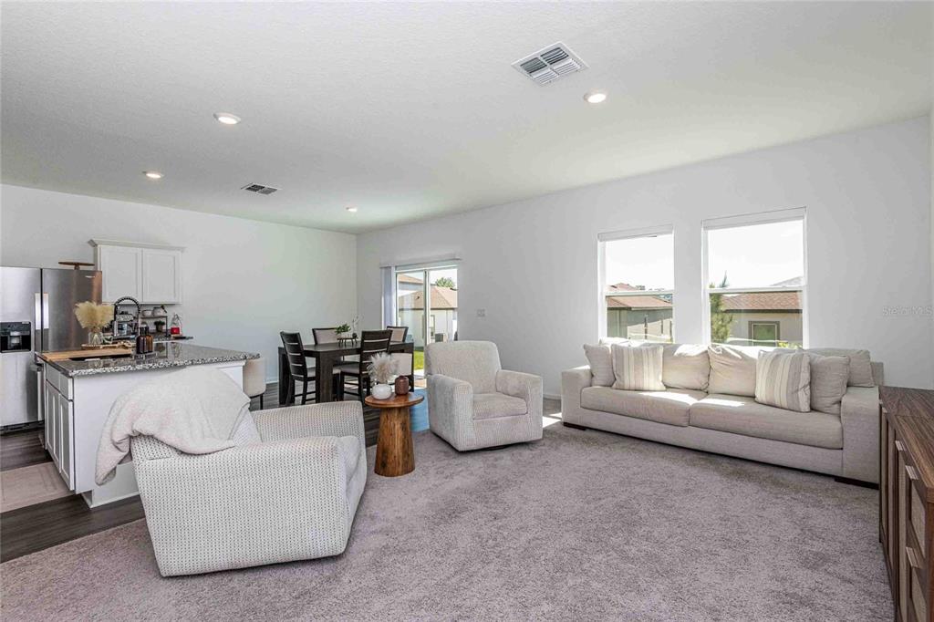 An open-concept living room features a kitchen island, dining area, and neutral-toned furniture — 11644 JUDICIAL COURT, DADE CITY, FL