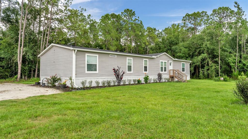 A single-story manufactured home with light gray siding sits on a grassy lot near trees — 12615 OLD DADE CITY ROAD, KATHLEEN, FL