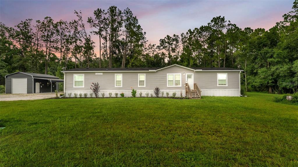 A single-story manufactured home with gray siding stands on a grassy lot near trees — 12615 OLD DADE CITY ROAD, KATHLEEN, FL
