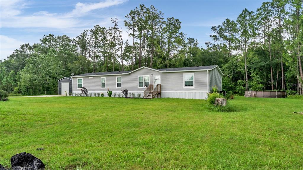 A single-story manufactured home with gray siding sits on a large, grassy lot with trees — 12615 OLD DADE CITY ROAD, KATHLEEN, FL