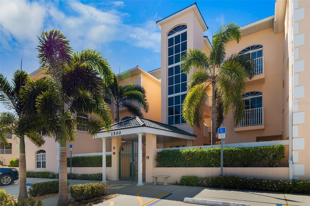 A multi-story peach-colored apartment building features a gated entrance, palm trees, and a parking lot — 1522 GONDOLA PARK DRIVE UNIT 1522, VENICE, FL