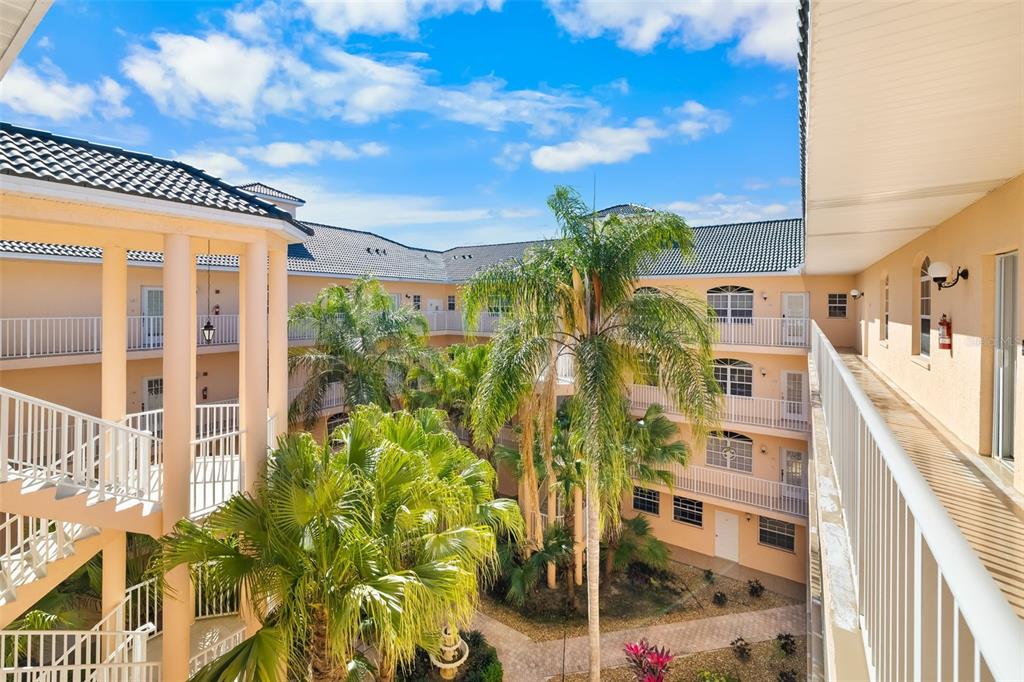 An exterior view of a multi-story apartment complex courtyard with palm trees and walkways — 1522 GONDOLA PARK DRIVE UNIT 1522, VENICE, FL
