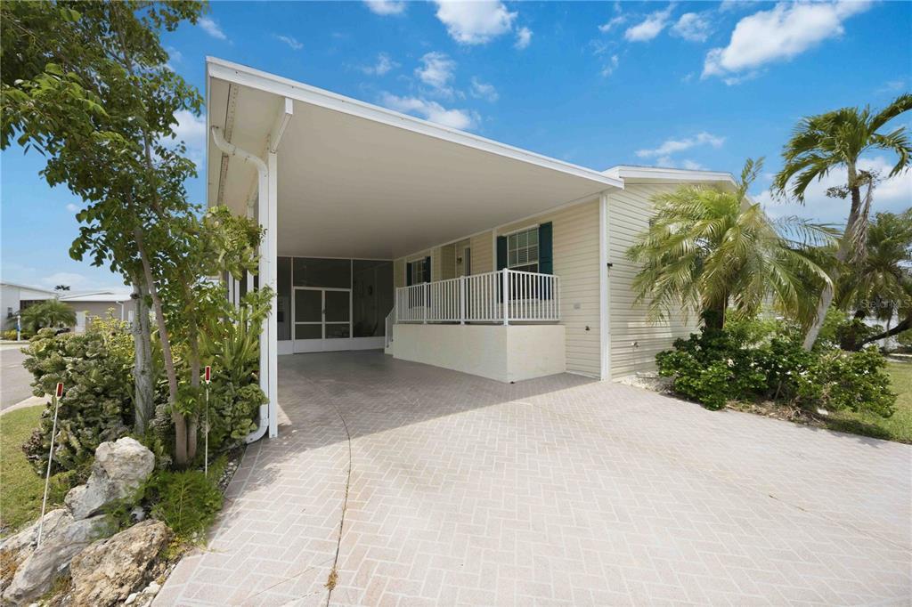 A covered carport with a brick-patterned floor leads to a raised porch and front entrance — 18 EMDEN CIRCLE, PUNTA GORDA, FL