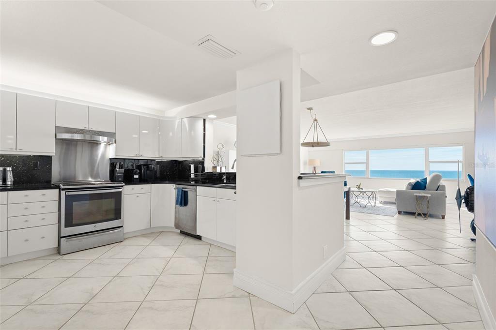 A modern kitchen with white cabinets and black countertops opens to a living area with ocean views — 1750 BENJAMIN FRANKLIN DRIVE UNIT 8D, SARASOTA, FL