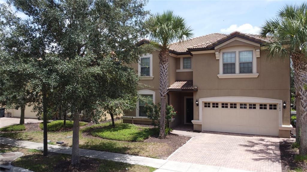 A two-story tan stucco house with a tiled roof, palm trees, and a paved driveway — 2183 TRIPOLI CT, KISSIMMEE, FL
