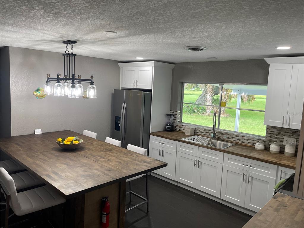 A kitchen features white cabinetry, dark wood countertops, a large island, and a stainless refrigerator — 2101 PALM BOULEVARD, MELBOURNE, FL