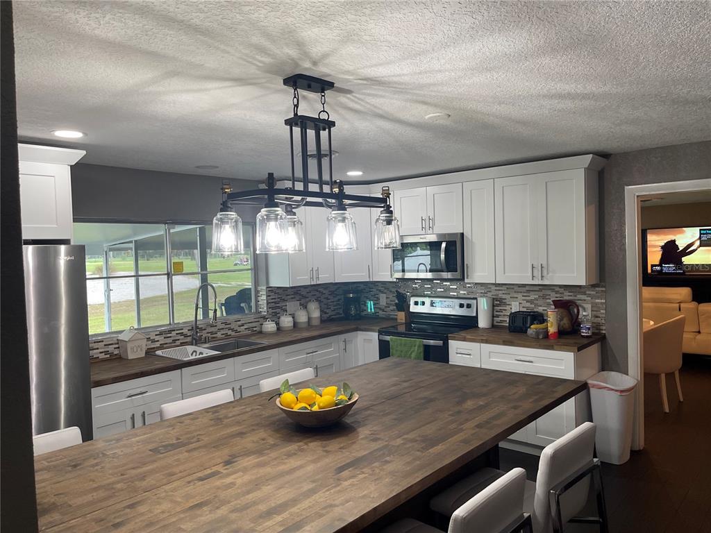 A kitchen features white cabinets, dark wood countertops, a large island, and a hanging light fixture — 2101 PALM BOULEVARD, MELBOURNE, FL