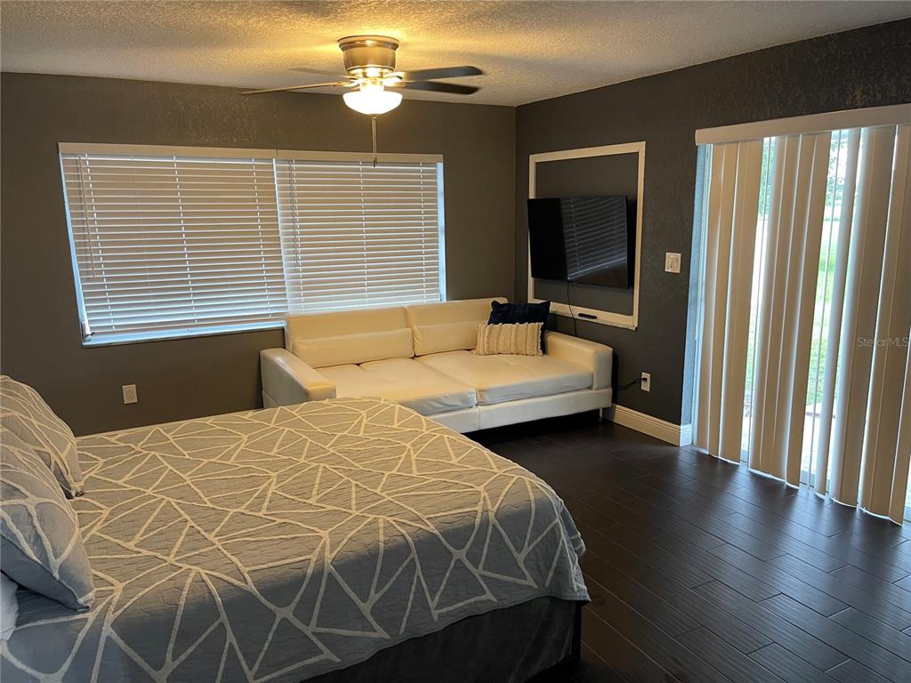 A bedroom features a bed, a white sofa, a wall-mounted television, and dark tile flooring — 2101 PALM BOULEVARD, MELBOURNE, FL