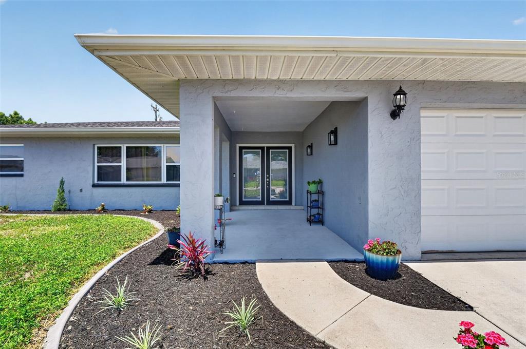 A gray house exterior features a covered entryway with double glass doors and a garage — 1305 SE 37TH TERRACE, CAPE CORAL, FL