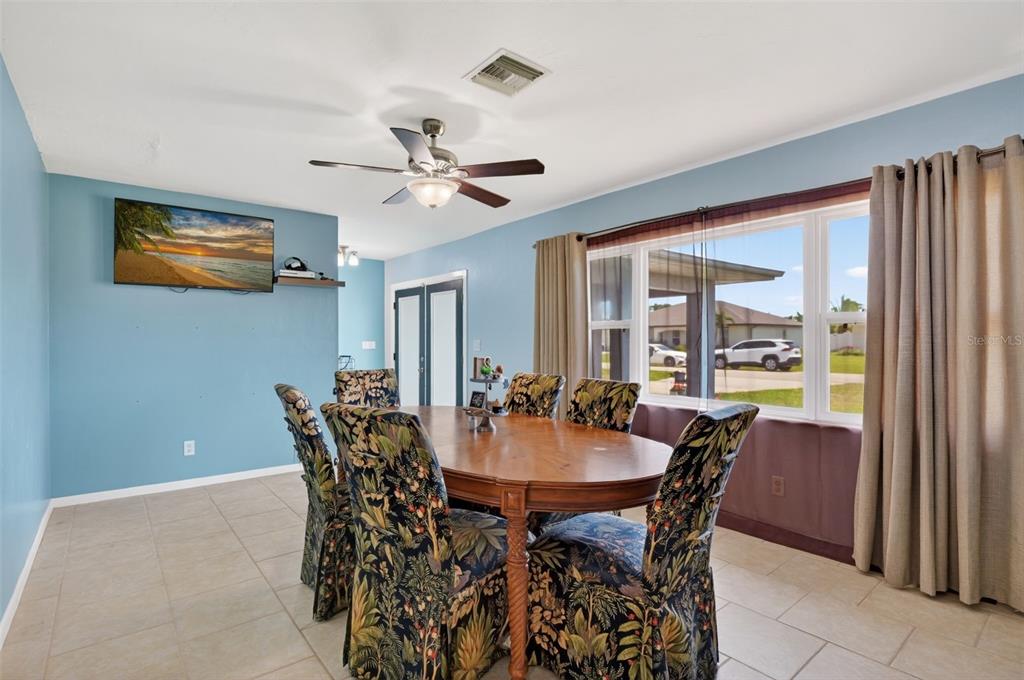 A dining room features a wooden table, patterned chairs, blue walls, and a large window — 1305 SE 37TH TERRACE, CAPE CORAL, FL