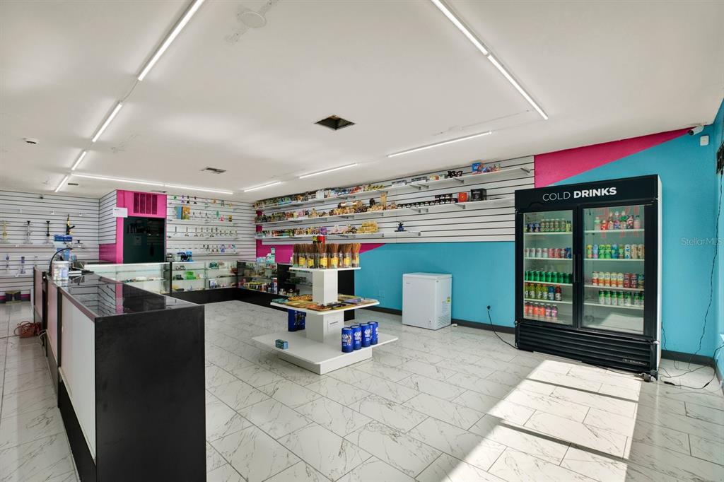 A retail store interior features white slat walls, a cold drinks refrigerator, and tiled flooring — N 49TH, PINELLAS PARK, FL