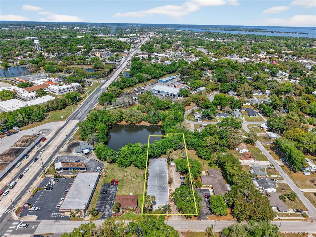 An aerial view shows a commercial building highlighted by a yellow outline near a pond — 1314 SUMTER STREET, LEESBURG, FL