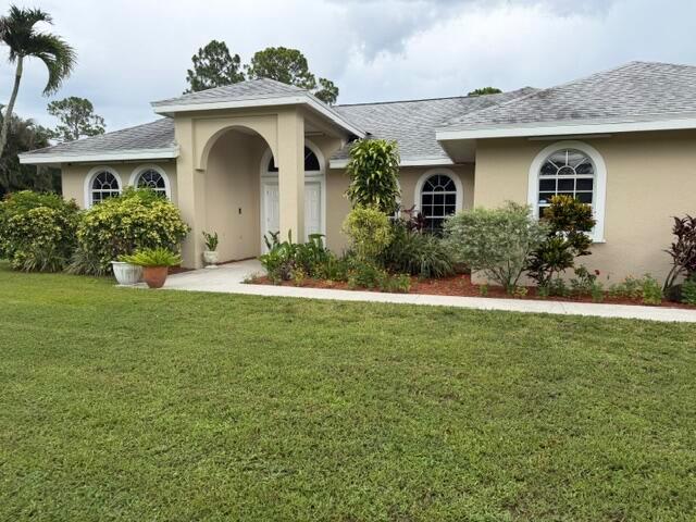 A single-story beige house with an arched entryway and arched windows sits behind a lawn — 16304 Orange Boulevard, FL 33470, FL
