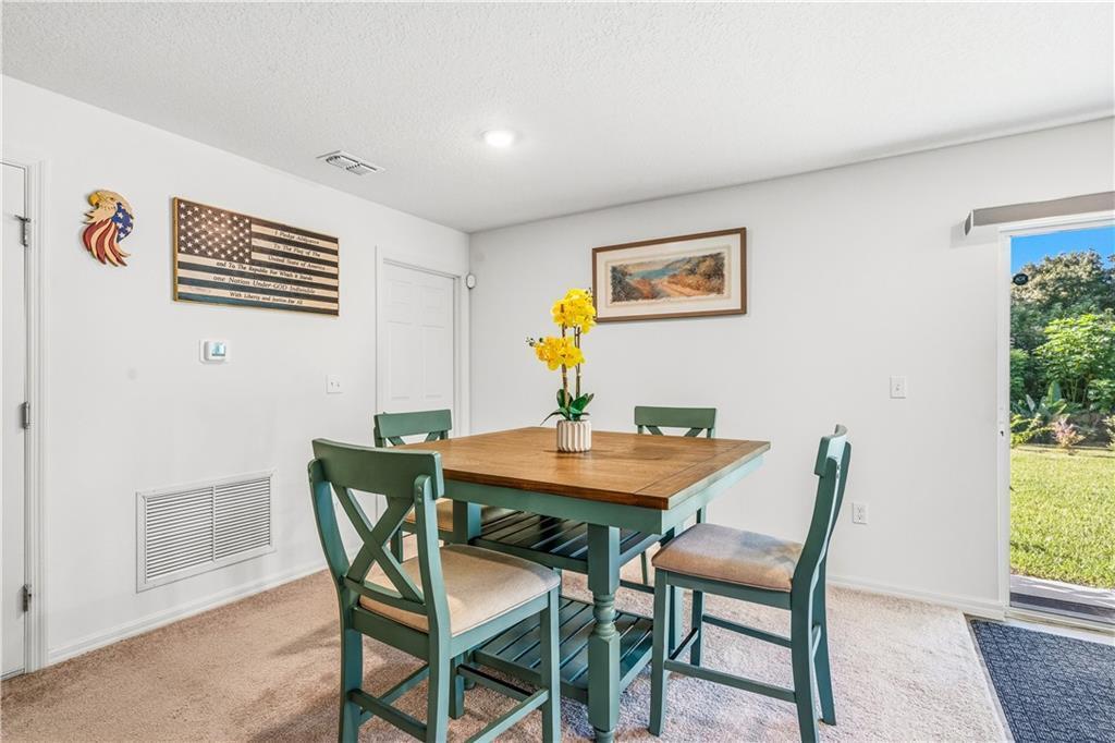 A dining area features a square wooden table with green chairs and a sliding glass door — SEBASTIAN, FL