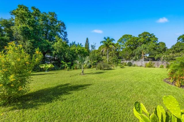 A large, grassy backyard features various trees, shrubs, and a wooden fence in the distance — SEBASTIAN, FL