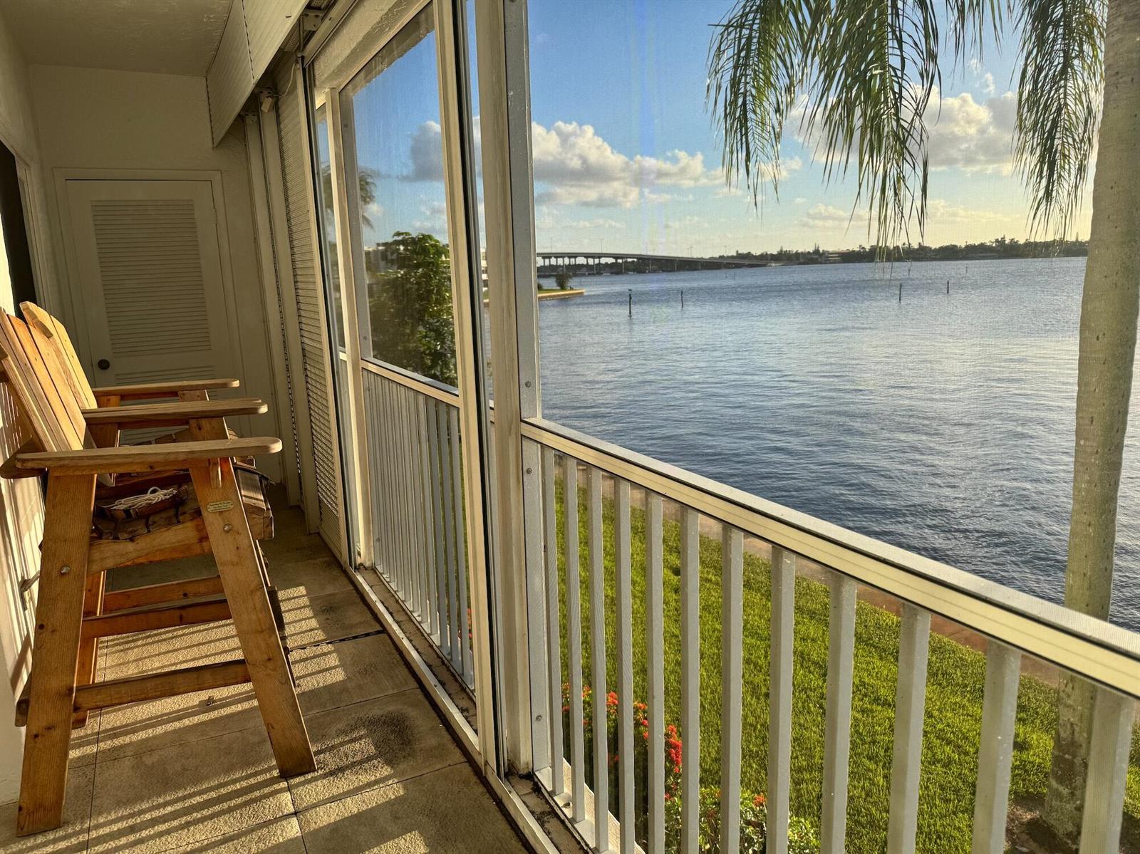 A screened-in balcony features wooden chairs overlooking a body of water and a distant bridge — 1868 SW Palm City Road # 202, Stuart FL 34994, STUART, FL
