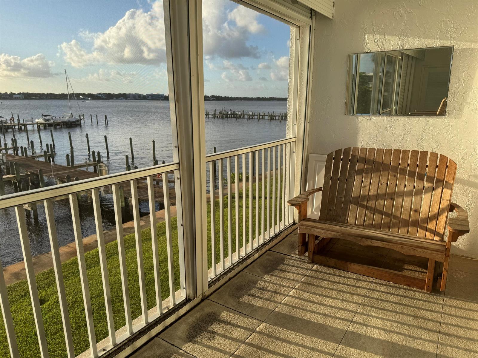A screened-in porch features a wooden bench, tile flooring, and a view of the water — 1868 SW Palm City Road # 202, Stuart FL 34994, STUART, FL