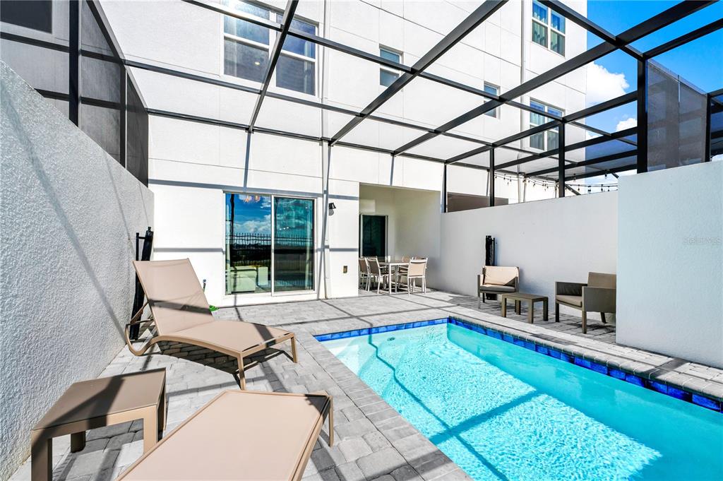 A screened-in patio features a rectangular swimming pool, lounge chairs, and outdoor dining furniture — 412 FAMAGUSTA, DAVENPORT, FL