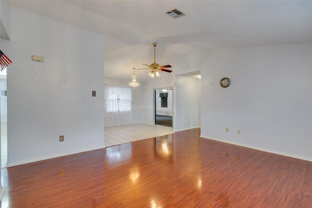 A living room with wood-look flooring leads to a tiled dining area with a chandelier — 7300 BEARDSLEY STREET, ENGLEWOOD, FL