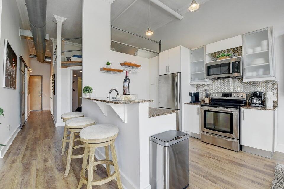 A kitchen with stainless steel appliances, white cabinetry, a granite breakfast bar, and wood flooring — 185 NE 4th Avenue # 210, Delray Beach FL 33483, DELRAY BEACH, FL