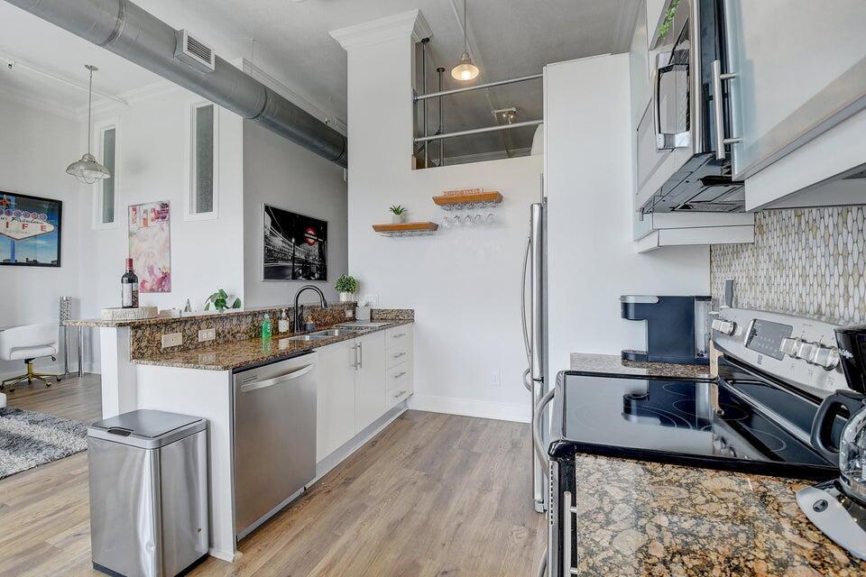 A modern kitchen features granite countertops, white cabinetry, stainless steel appliances, and wood-look flooring — 185 NE 4th Avenue # 210, Delray Beach FL 33483, DELRAY BEACH, FL