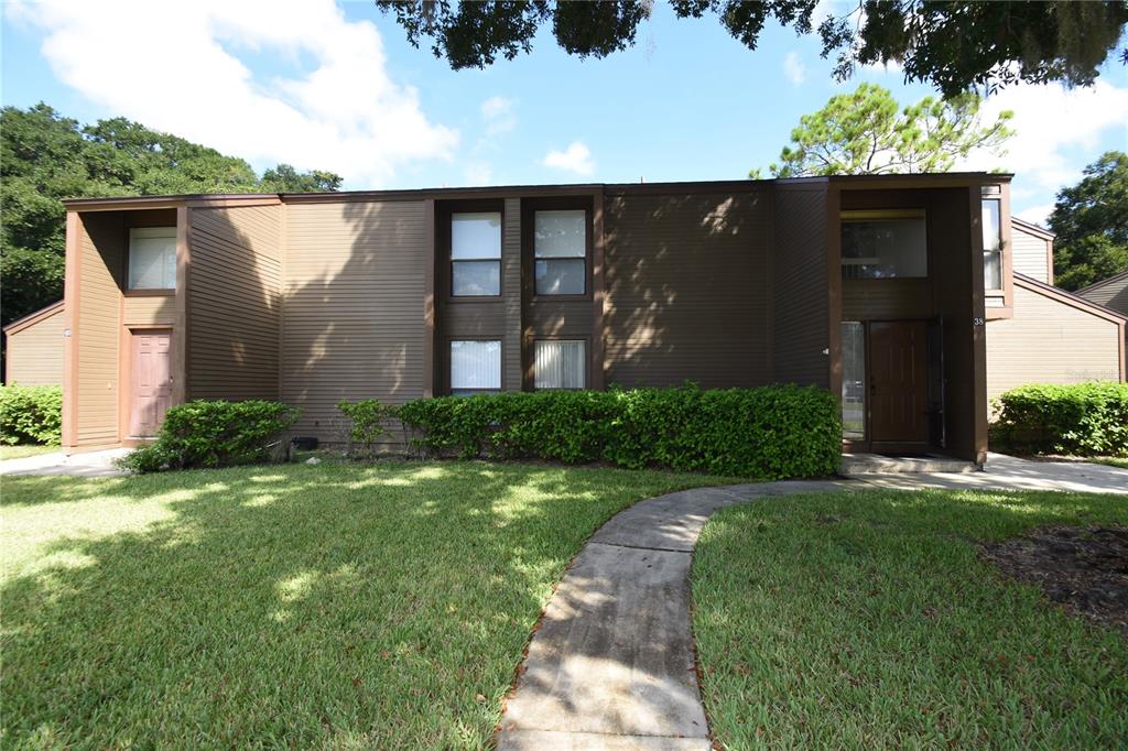A two-story brown building with horizontal siding, a concrete walkway, and a manicured hedge — 38 OXFORD LANE UNIT 38, PALM COAST, FL