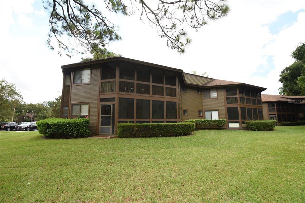 A two-story brown apartment building features screened-in porches and is surrounded by a grassy lawn — 38 OXFORD LANE UNIT 38, PALM COAST, FL