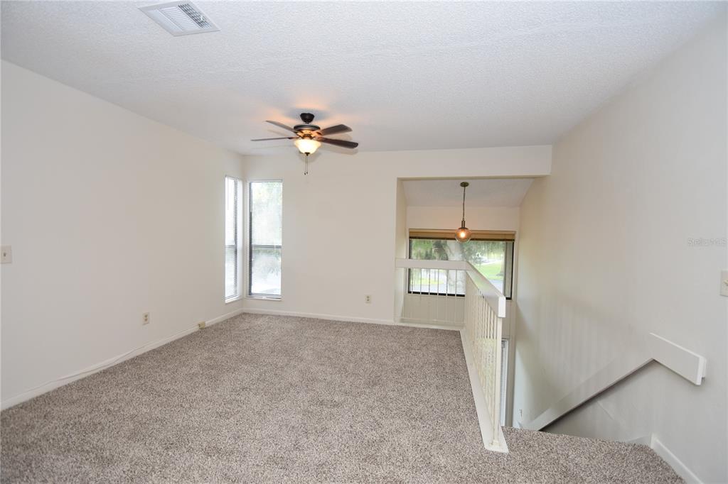 A carpeted loft area features a ceiling fan, a white railing, and a staircase — 38 OXFORD LANE UNIT 38, PALM COAST, FL