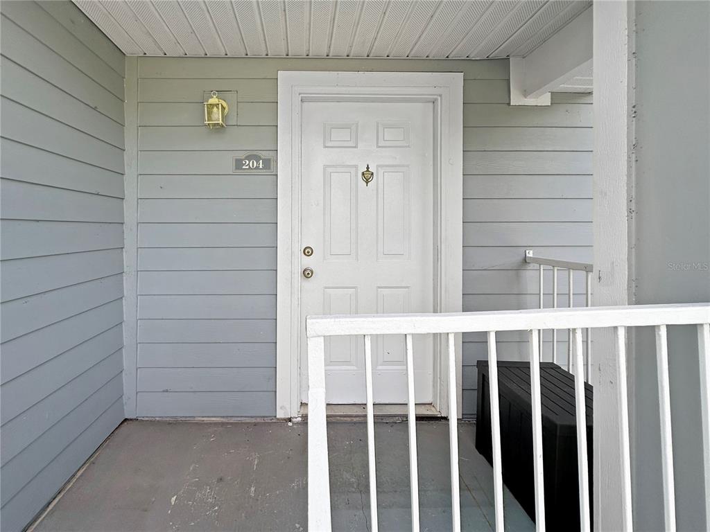 A white front door with a brass knocker is set into light gray horizontal siding — 708 SECRET HARBOR LANE UNIT 204, LAKE MARY, FL