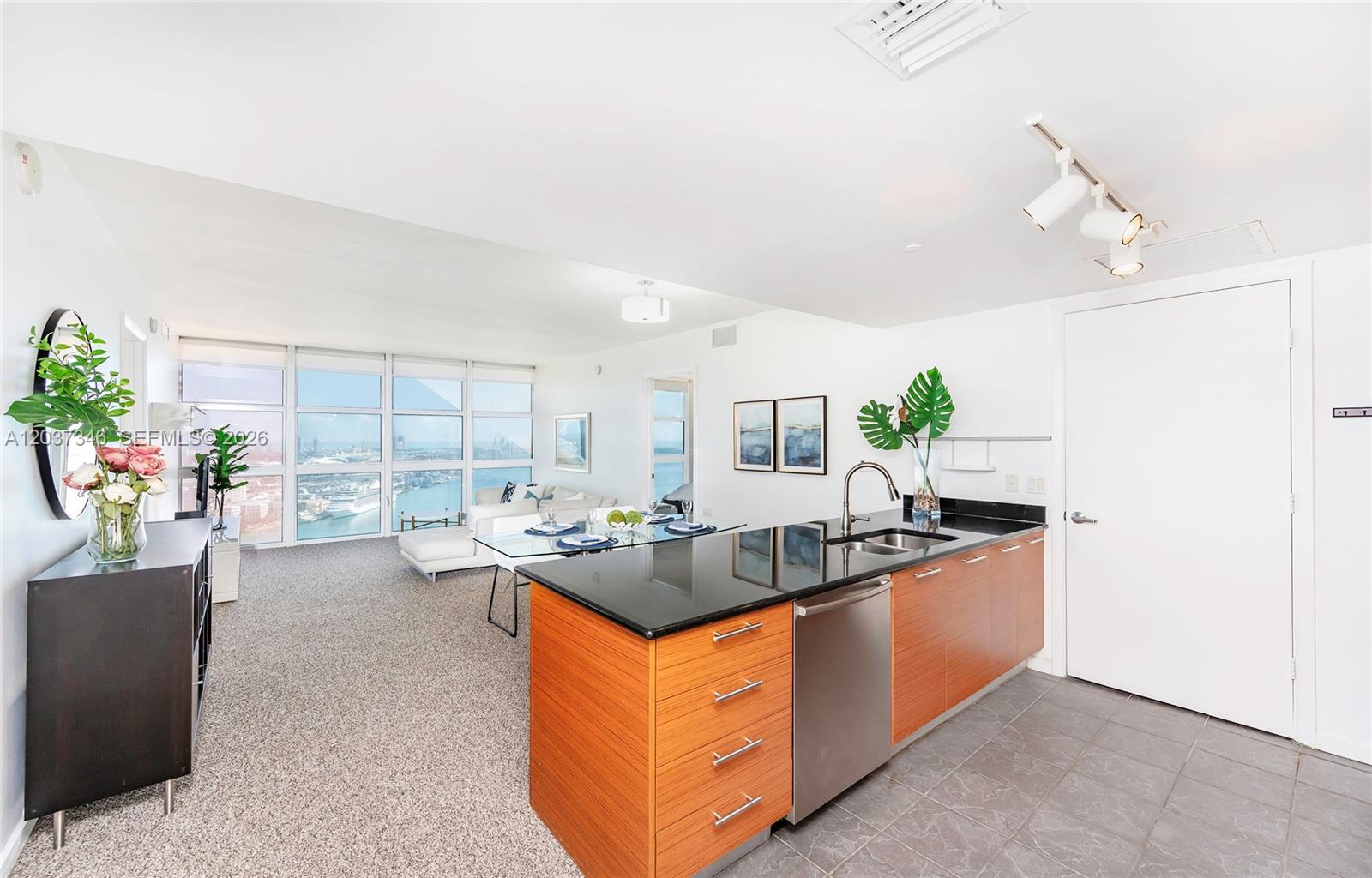 A modern kitchen with wood cabinets and a black countertop opens to a living area — 50 Biscayne Blvd # 4104, Miami FL 33132, MIAMI, FL