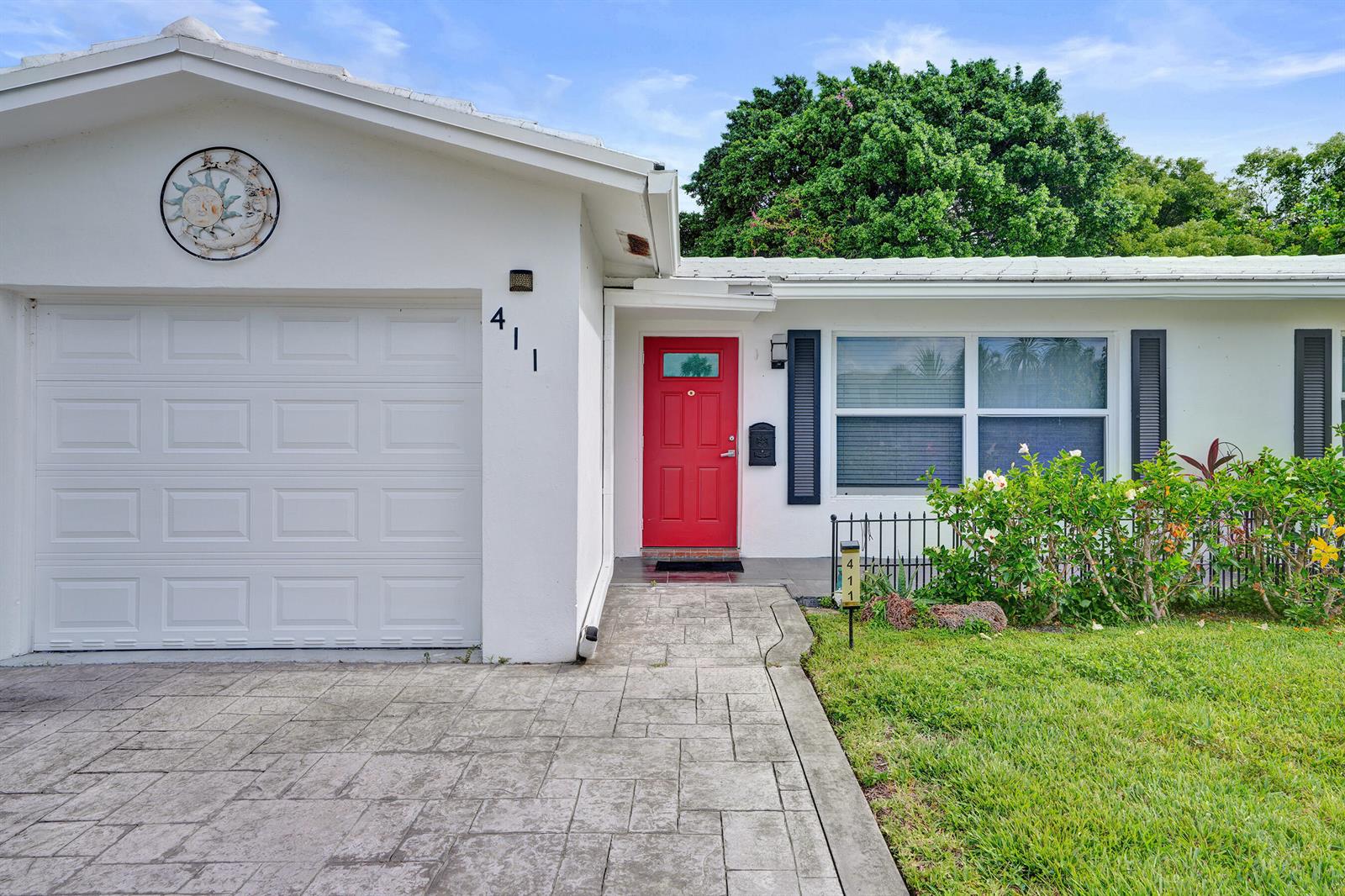 A white house exterior features a red front door, a garage, and a paved walkway — 411 NW 26th Court, Pompano Beach FL 33064, POMPANO BEACH, FL