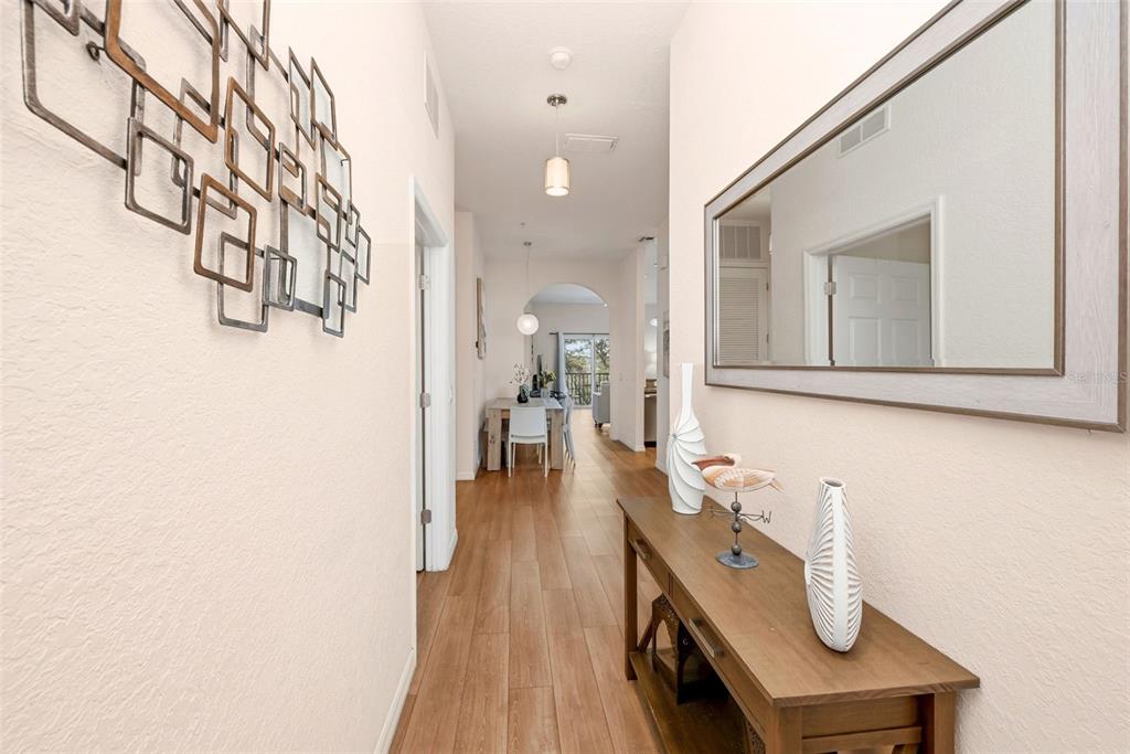 A hallway features wood-look flooring, a console table with decor, a wall mirror, and artwork — 1014 GRAN BAHAMA BOULEVARD UNIT 31-1014, DAVENPORT, FL
