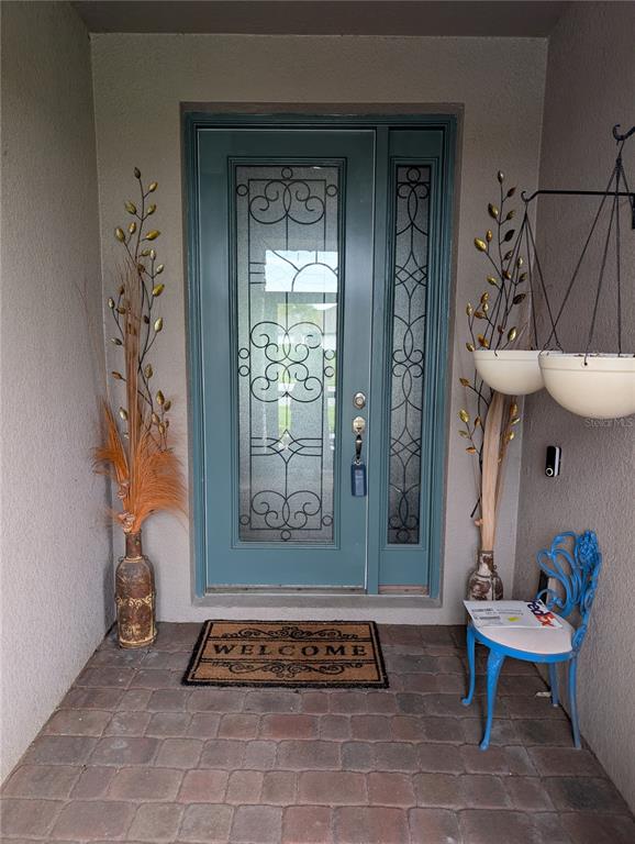 A front entryway features a teal door with decorative glass, a welcome mat, and potted plants — 285 BELLA CORTINA DRIVE, POINCIANA, FL