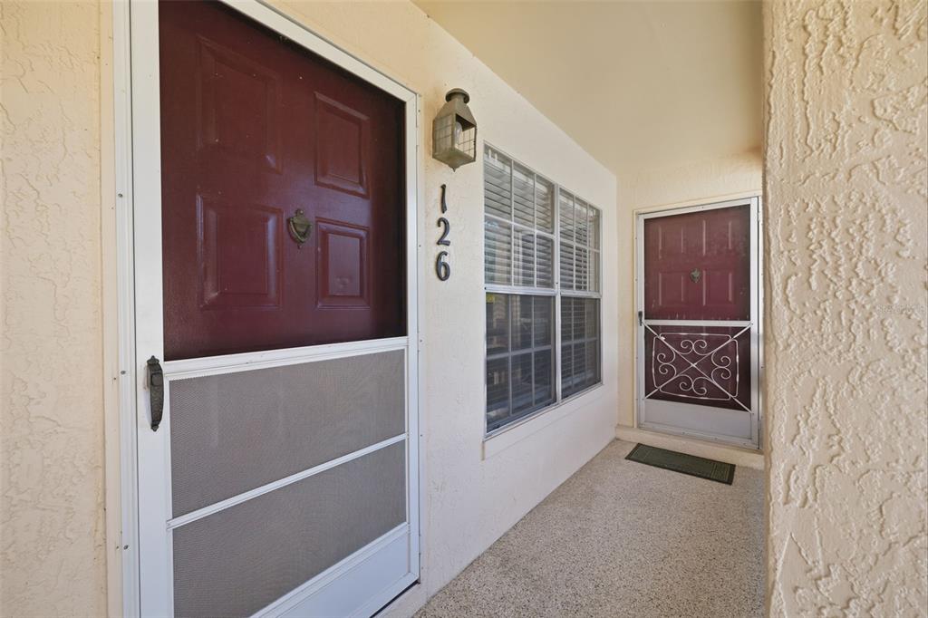 A covered entryway features two red front doors with screen doors and a house number — 7807 HARDWICK DRIVE UNIT 126, NEW PORT RICHEY, FL