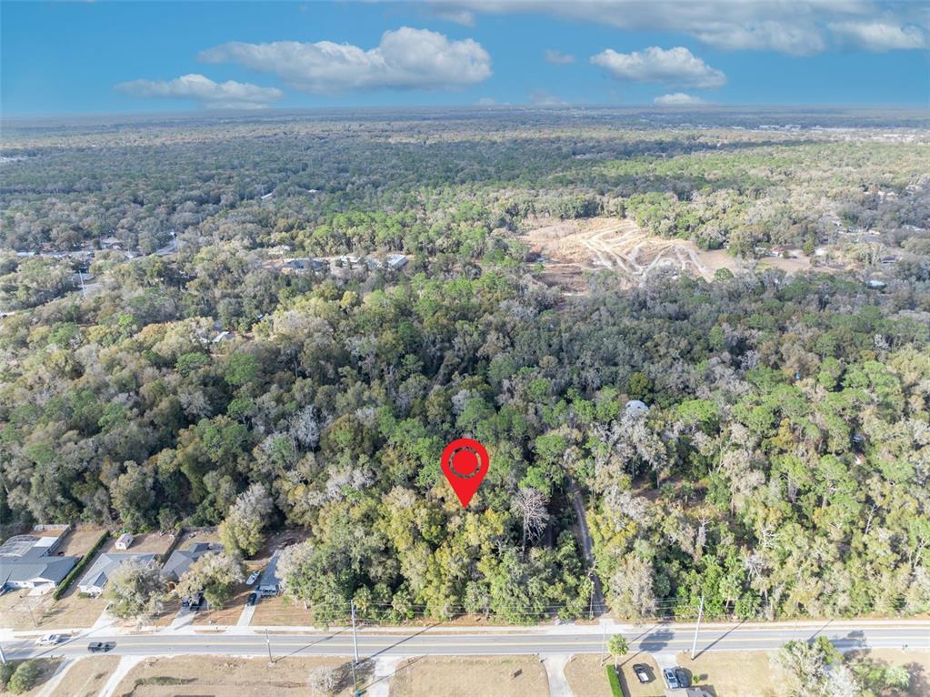 An aerial view shows a wooded lot marked with a red pin near a road — W NEW YORK AVENUE, ORANGE CITY, FL