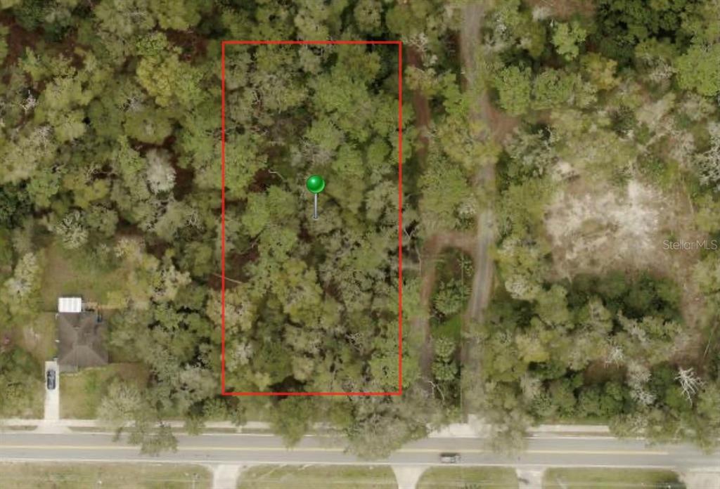 An aerial view shows a rectangular, tree-covered vacant lot outlined in red along a road — W NEW YORK AVENUE, ORANGE CITY, FL