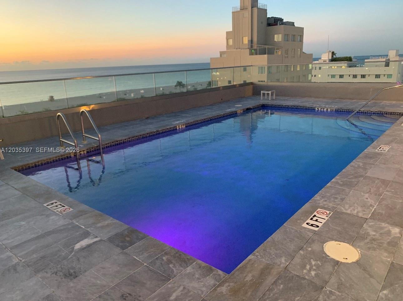 A rooftop swimming pool overlooks the ocean at sunset with a glass railing — 1255 Collins Ave # 208, Miami Beach FL 33139, MIAMI BEACH, FL