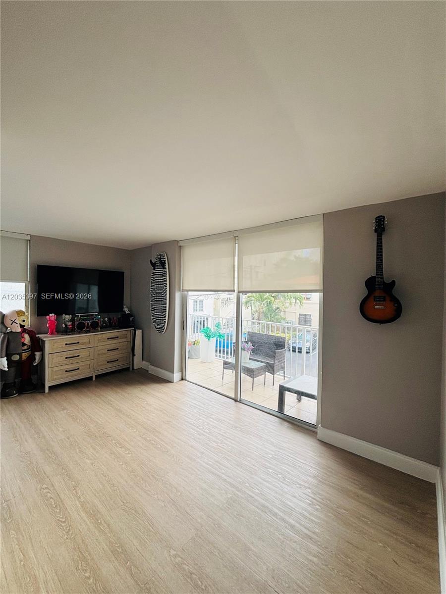A living room features light wood-look flooring, a television console, and a balcony with seating — 1255 Collins Ave # 208, Miami Beach FL 33139, MIAMI BEACH, FL