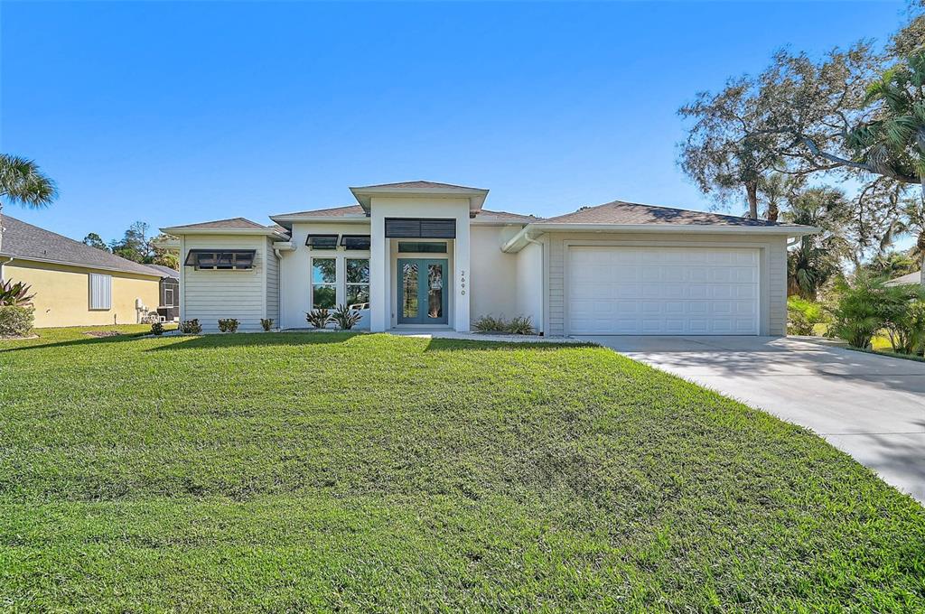 A single-story house with a light-colored exterior, a two-car garage, and a green lawn — 2690 PEBBLE CREEK PLACE, PORT CHARLOTTE, FL
